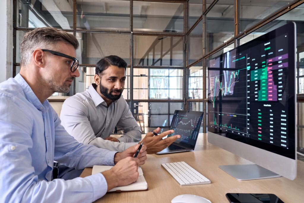 Deux hommes regardant un écran d'ordinateur avec des graphiques et des projections d'investissement.