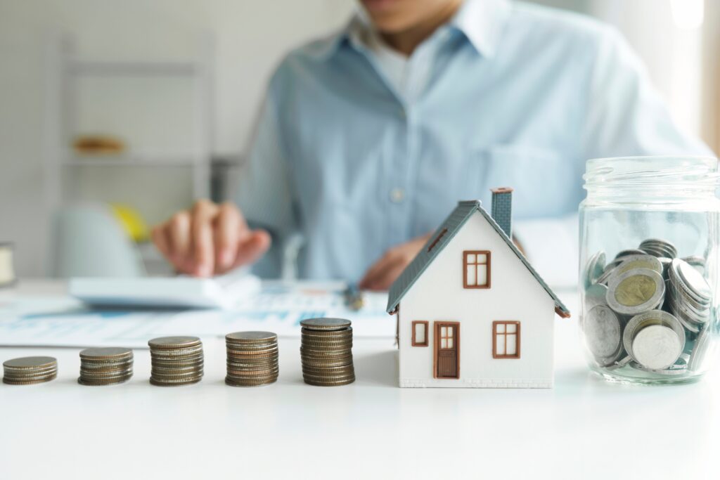 Person looking into private lending investments with stacks of coins beside a house figurine